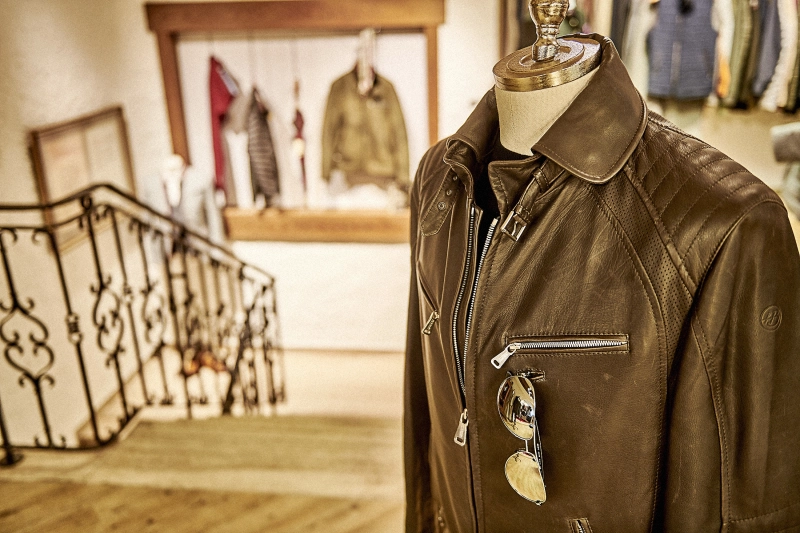 stilvolle braune Lederjacke mit eingehängter Pilotensollenbrille vor der Treppe im Geschäft